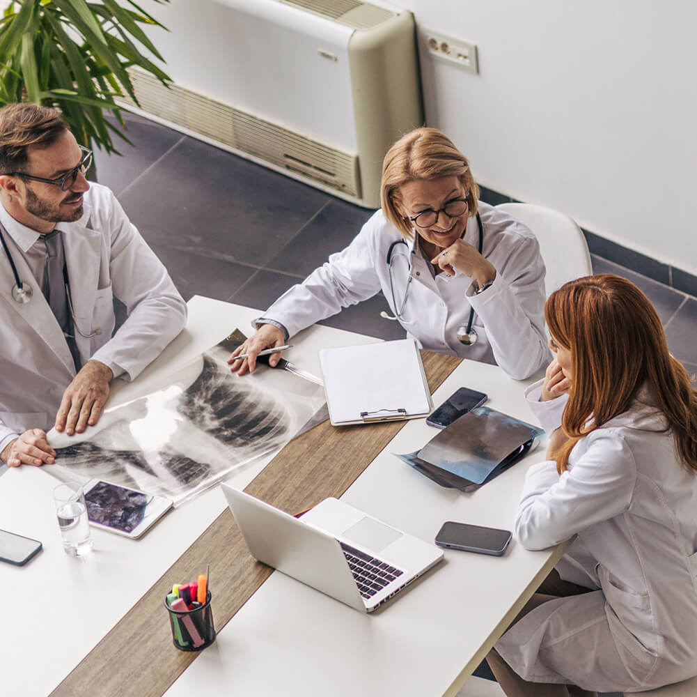 Three doctors in white coats review an X-ray